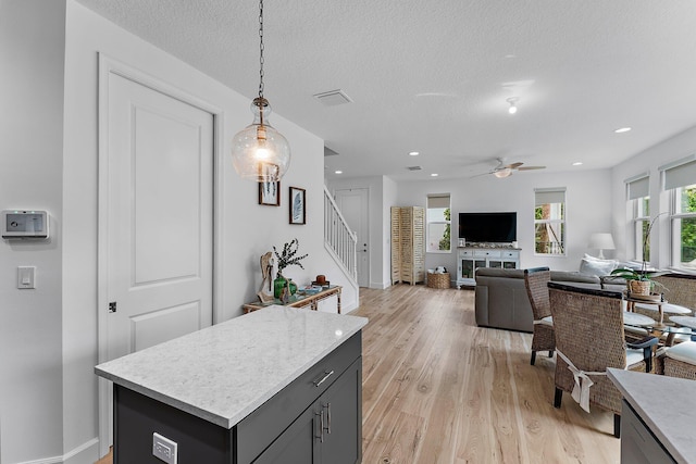 interior space with a ceiling fan, light wood finished floors, a textured ceiling, decorative light fixtures, and open floor plan