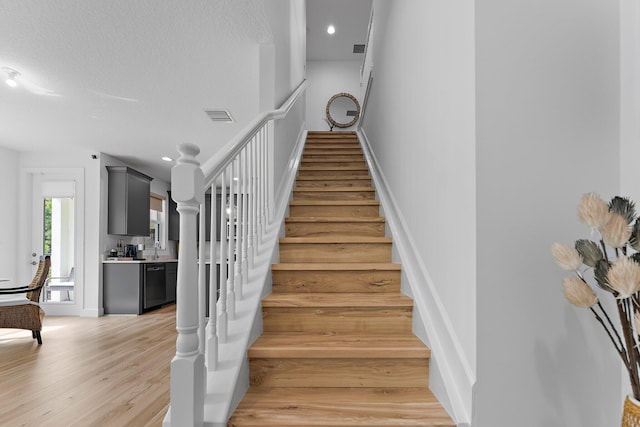 stairway with recessed lighting, wood finished floors, visible vents, and a textured ceiling