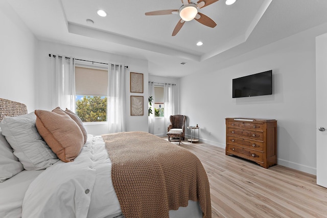 bedroom with recessed lighting, light wood-style flooring, a raised ceiling, and baseboards