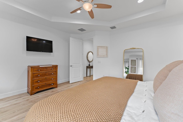 bedroom featuring visible vents, a ceiling fan, a tray ceiling, wood finished floors, and baseboards