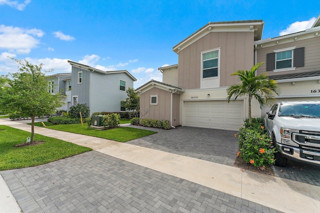 multi unit property with central air condition unit, decorative driveway, board and batten siding, a front yard, and a garage