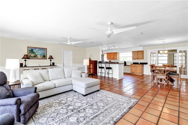 living area featuring light tile patterned floors, a textured ceiling, and ceiling fan with notable chandelier