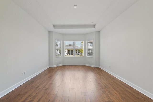 spare room featuring a tray ceiling, dark wood finished floors, and baseboards