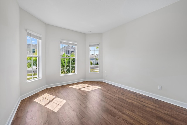 empty room with dark wood-type flooring, plenty of natural light, and baseboards