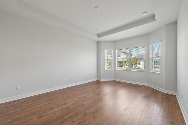 unfurnished room featuring dark wood-style flooring, a raised ceiling, and baseboards