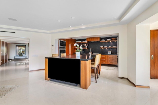 kitchen featuring wall oven, a raised ceiling, dark countertops, and brown cabinetry