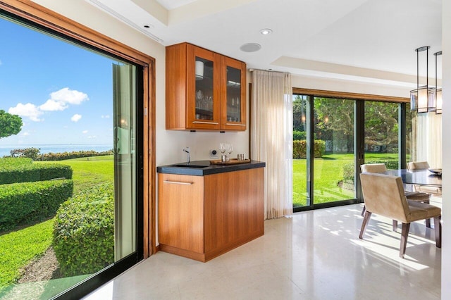 kitchen featuring glass insert cabinets, brown cabinets, dark countertops, and a raised ceiling