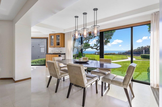 dining room with a tray ceiling, bar, baseboards, and a chandelier