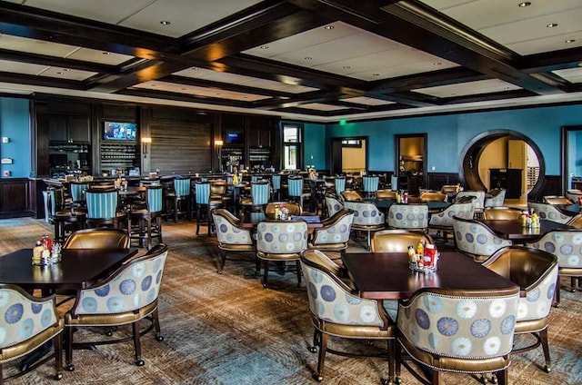 carpeted dining space featuring beamed ceiling, arched walkways, a wainscoted wall, and coffered ceiling