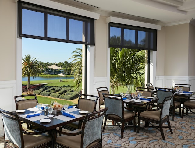 dining area featuring a decorative wall, wainscoting, crown molding, and a water view