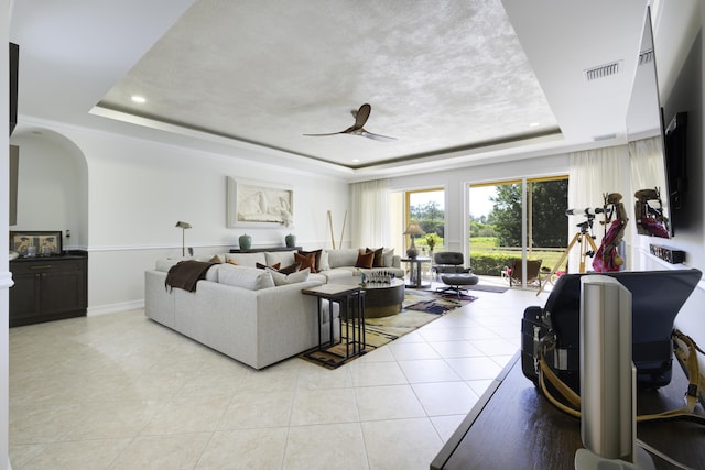 living room featuring a raised ceiling, light tile patterned flooring, visible vents, and ceiling fan