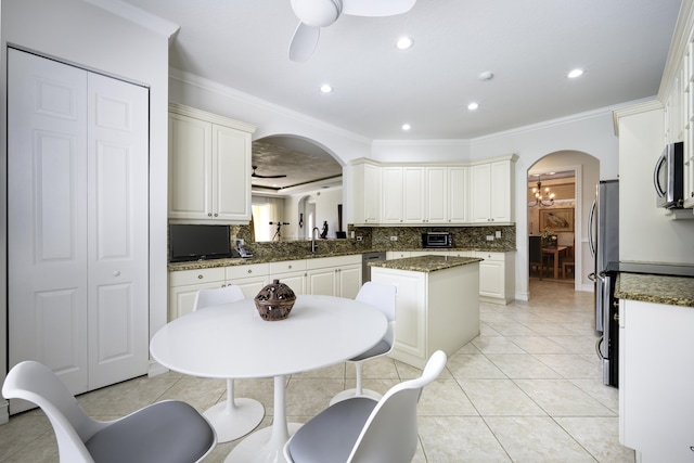 kitchen featuring arched walkways, a sink, decorative backsplash, ceiling fan, and stainless steel microwave