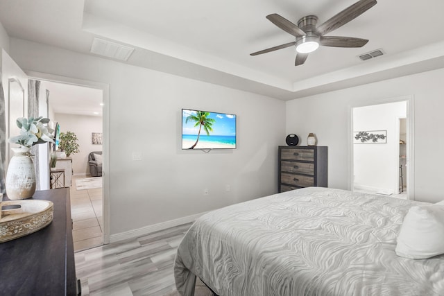 bedroom with light wood-type flooring, a raised ceiling, visible vents, and baseboards