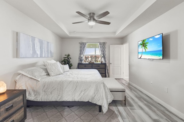 bedroom with wood finished floors, a raised ceiling, a ceiling fan, and baseboards