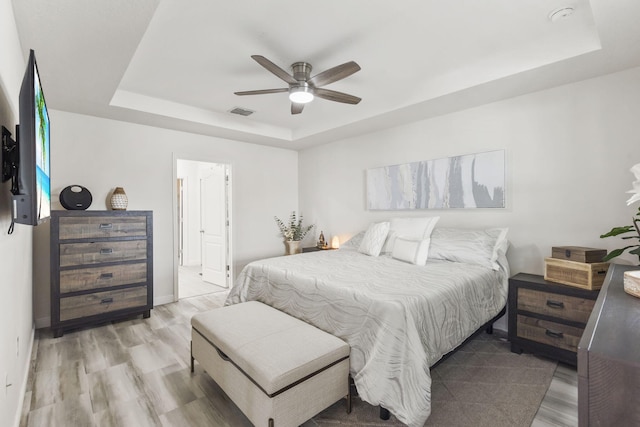 bedroom with a tray ceiling, visible vents, and light wood-style floors