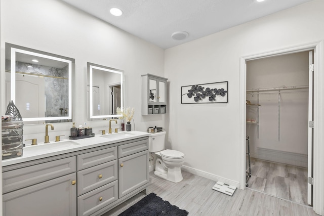 full bath with toilet, double vanity, baseboards, and a sink