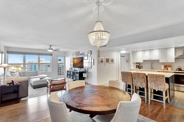 dining room with ceiling fan with notable chandelier, a textured ceiling, light wood-type flooring, and baseboards