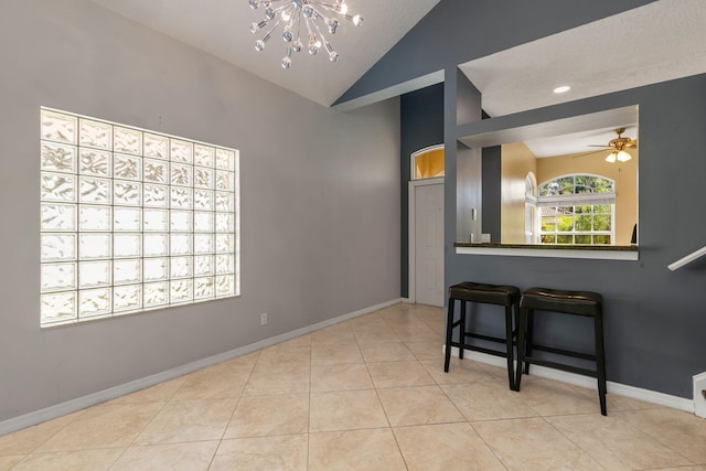 spare room with high vaulted ceiling, ceiling fan with notable chandelier, baseboards, and tile patterned floors