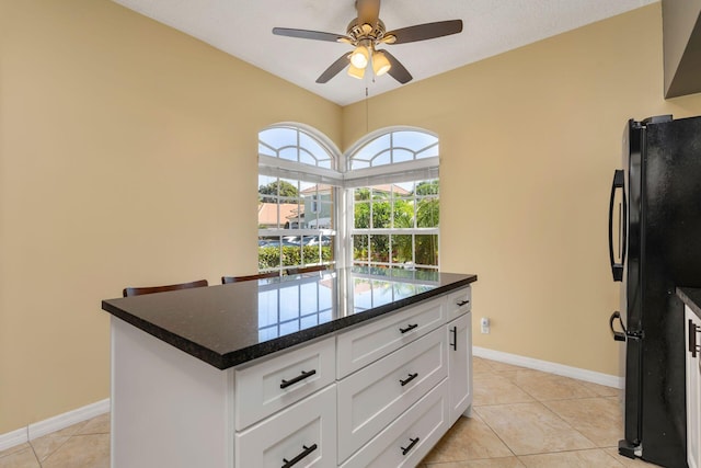 kitchen with freestanding refrigerator, white cabinetry, ceiling fan, light tile patterned flooring, and baseboards