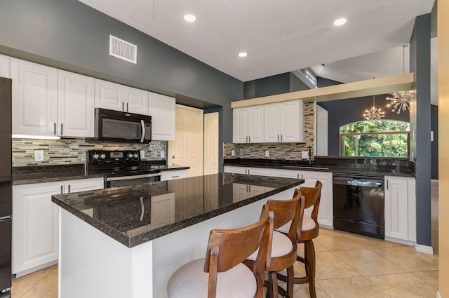 kitchen with a breakfast bar, visible vents, white cabinets, backsplash, and black appliances