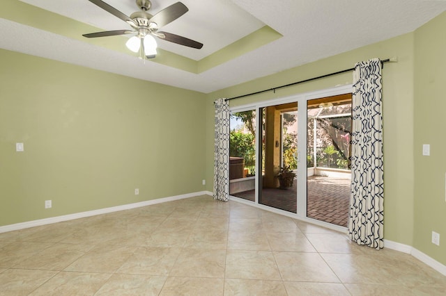 spare room featuring ceiling fan, light tile patterned floors, a raised ceiling, and baseboards