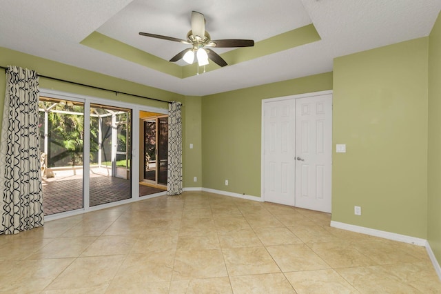 spare room with a tray ceiling, light tile patterned flooring, ceiling fan, and baseboards