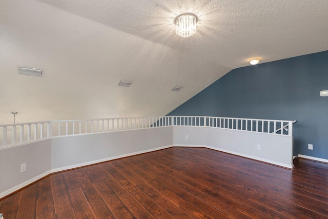 unfurnished room featuring wood-type flooring, visible vents, vaulted ceiling, and a textured ceiling