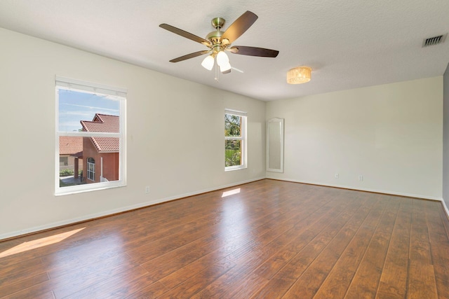 empty room with dark wood-style flooring, visible vents, and baseboards