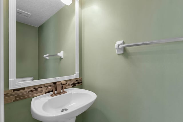 bathroom with a textured ceiling, visible vents, backsplash, and a sink