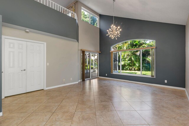 unfurnished living room featuring a chandelier, tile patterned flooring, a high ceiling, and baseboards