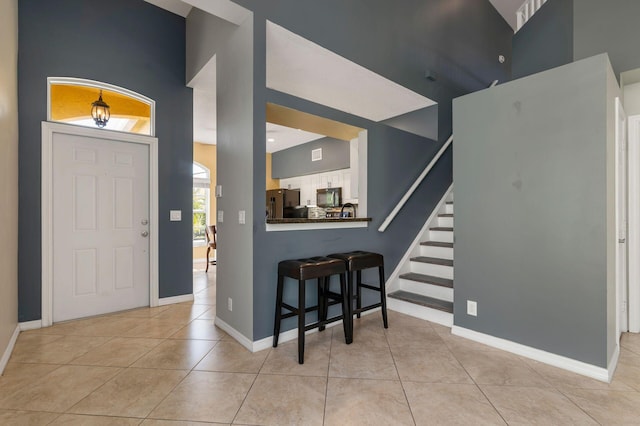 entryway with light tile patterned floors, a high ceiling, stairs, and baseboards