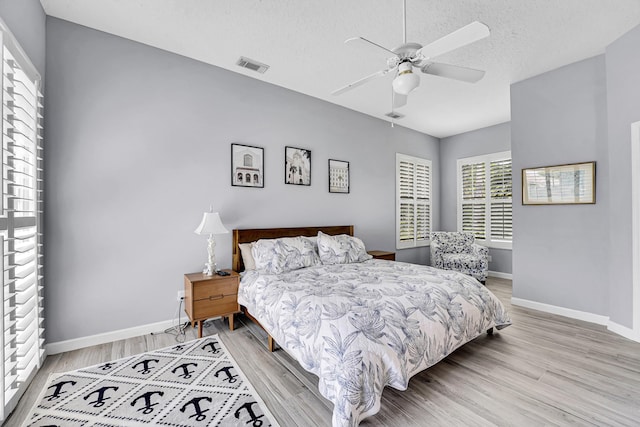 bedroom with visible vents, baseboards, light wood-style flooring, ceiling fan, and a textured ceiling