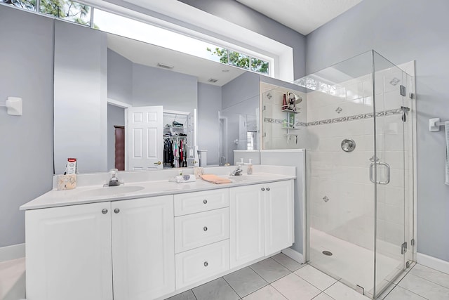 full bath featuring a walk in closet, double vanity, a stall shower, a sink, and tile patterned floors