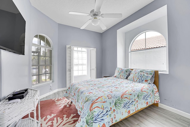 bedroom featuring ceiling fan, a textured ceiling, baseboards, and wood finished floors