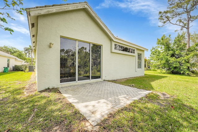 back of house featuring a patio area, a lawn, central AC unit, and stucco siding