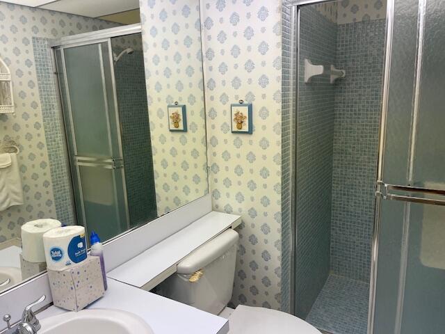 bathroom with wallpapered walls, vanity, toilet, and a shower stall
