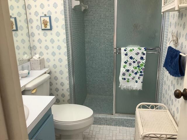 bathroom featuring wallpapered walls, vanity, toilet, and a shower stall