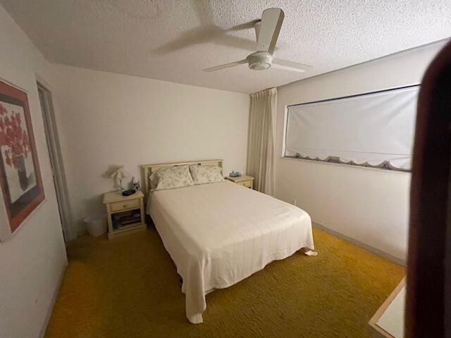 carpeted bedroom featuring ceiling fan and a textured ceiling