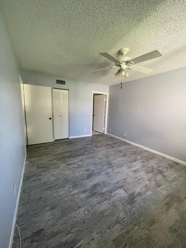 unfurnished bedroom featuring visible vents, ceiling fan, baseboards, dark wood-style floors, and a textured ceiling