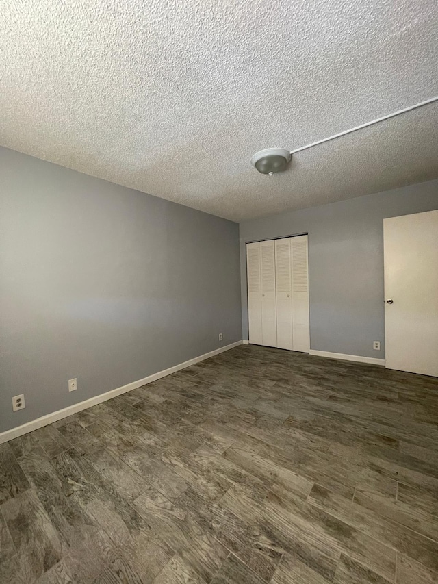 unfurnished bedroom with dark wood-style floors, a textured ceiling, baseboards, and a closet