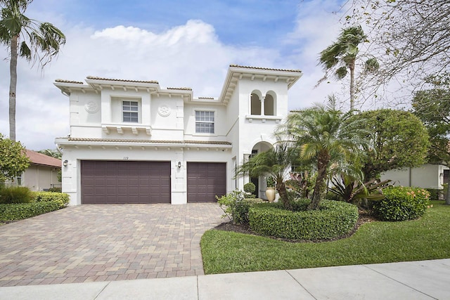 mediterranean / spanish house featuring a garage, decorative driveway, a tile roof, and stucco siding