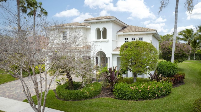 mediterranean / spanish home featuring a tiled roof, a front lawn, decorative driveway, and stucco siding