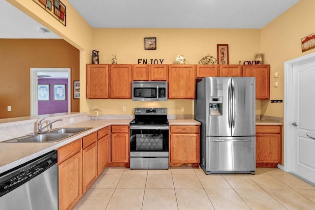 kitchen featuring light tile patterned flooring, a sink, light countertops, appliances with stainless steel finishes, and brown cabinets