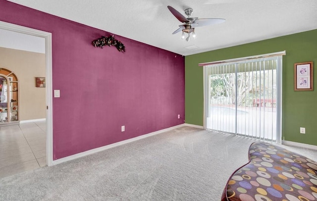 carpeted empty room featuring ceiling fan, a textured ceiling, baseboards, and tile patterned floors