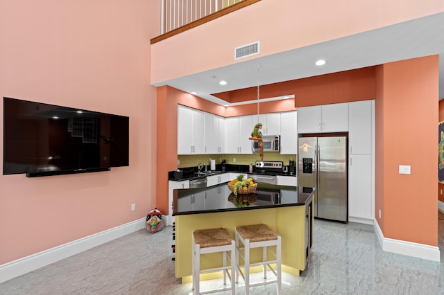 kitchen with stainless steel appliances, dark countertops, visible vents, baseboards, and a kitchen breakfast bar