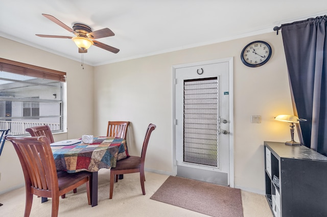 dining space featuring light colored carpet, baseboards, crown molding, and a ceiling fan