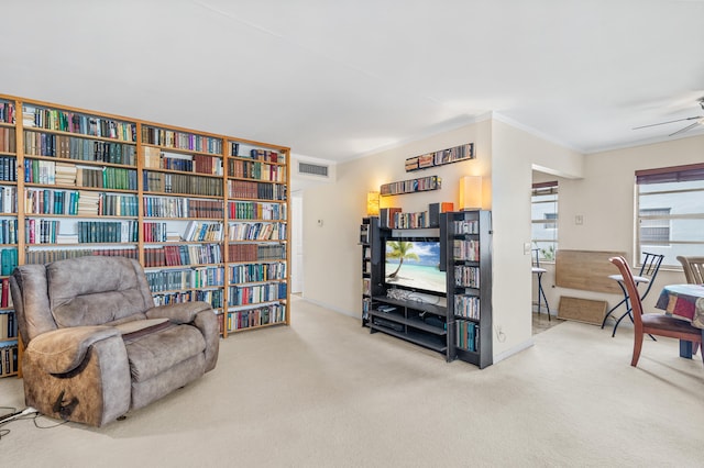 living area with a ceiling fan, visible vents, carpet floors, ornamental molding, and bookshelves