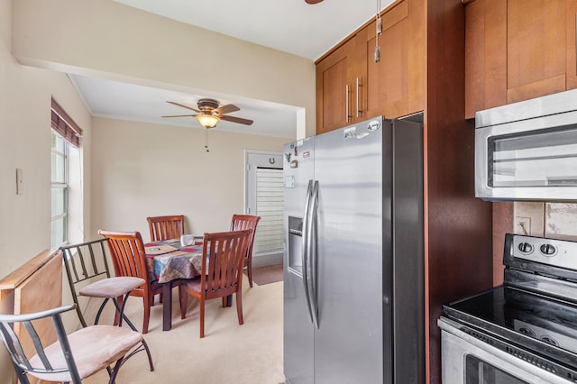 kitchen with a ceiling fan, brown cabinetry, appliances with stainless steel finishes, and light carpet