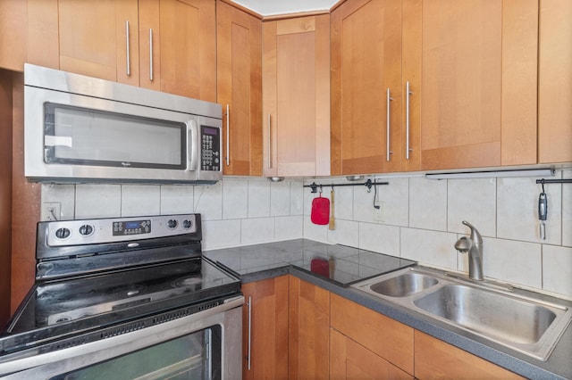 kitchen featuring dark countertops, backsplash, appliances with stainless steel finishes, and a sink