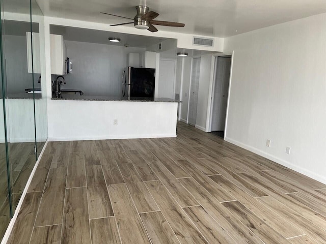 unfurnished living room with visible vents, ceiling fan, a sink, wood finished floors, and baseboards